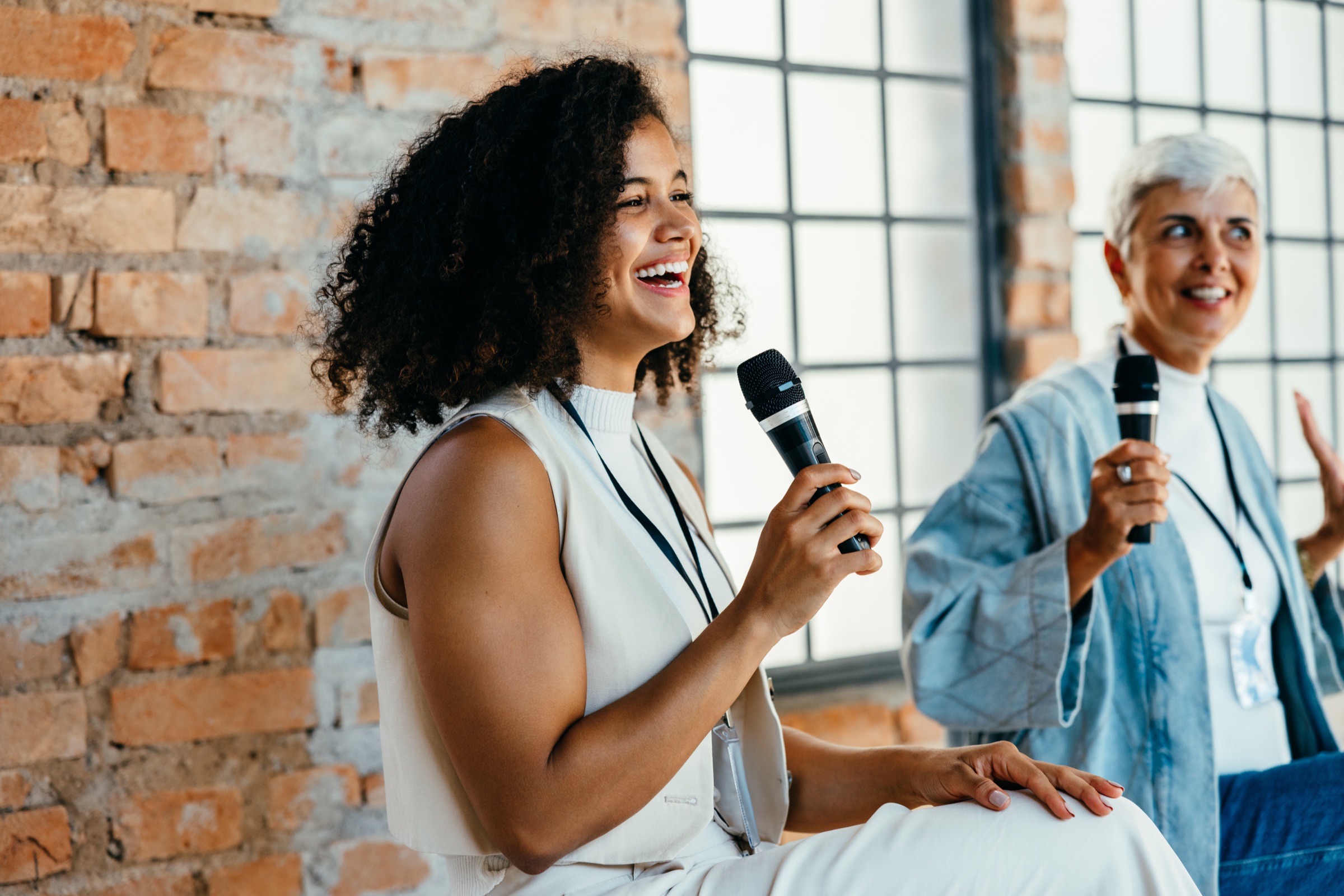 Women speaking on stage against a brick wall